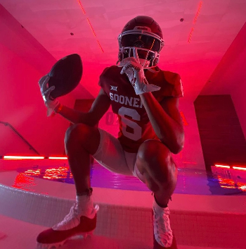 Football player in red and white gear posing in dramatic lighting.