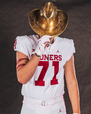 Football player in white jersey with number 77 and a sousaphone on his head.